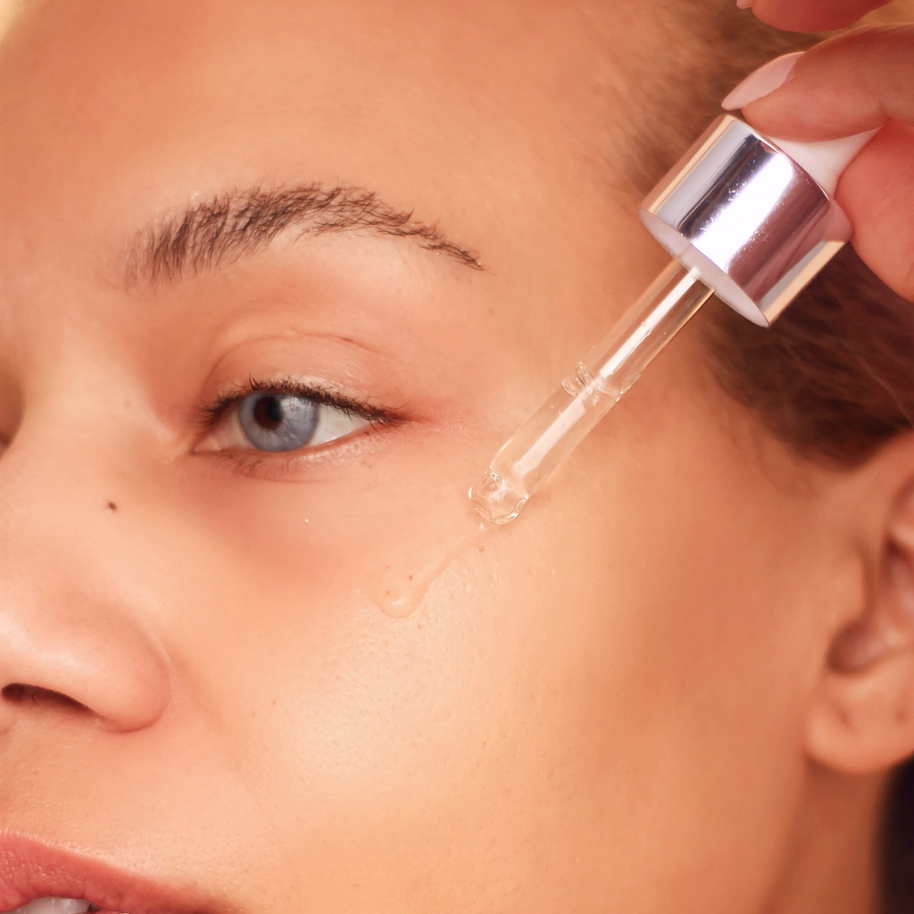 A woman using a dropper for a clear serum on her face