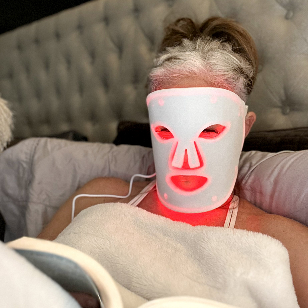 A woman is wearing a face mask with red lights while reading a book