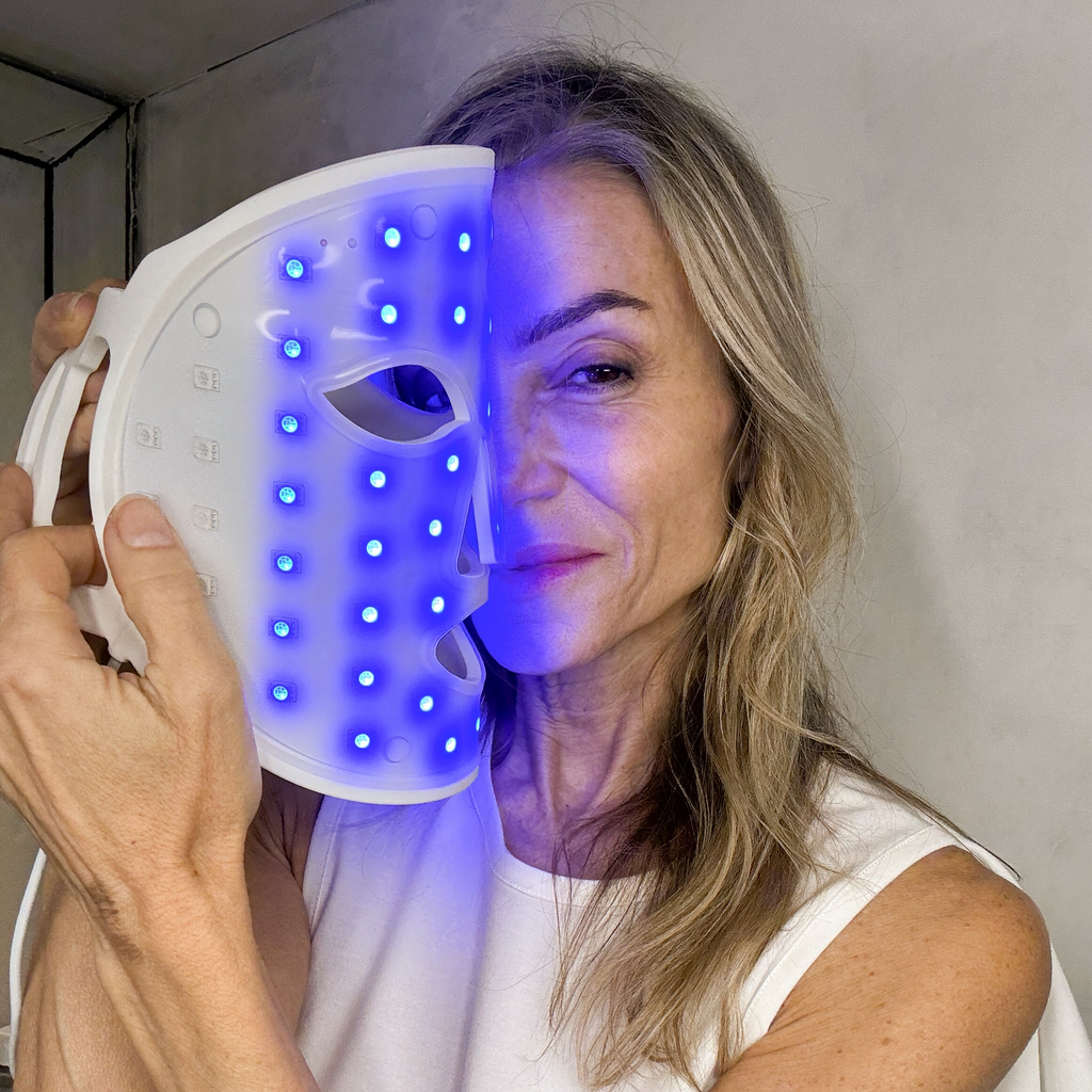 A woman is holding a face mask with blue light, covering half of her face