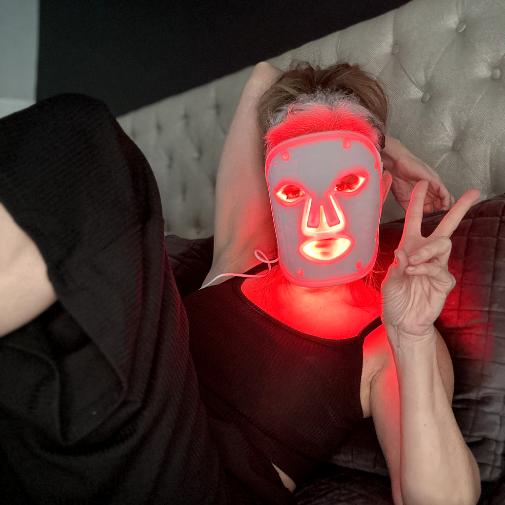 A woman is laying down while wearing a LED face mask.