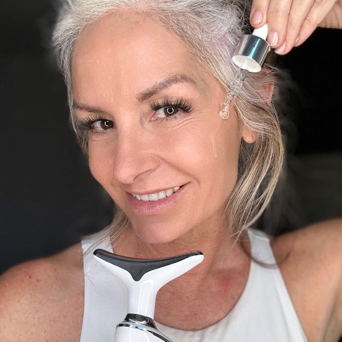 A woman using a serum dropper on her face while holding the MyoGlow.